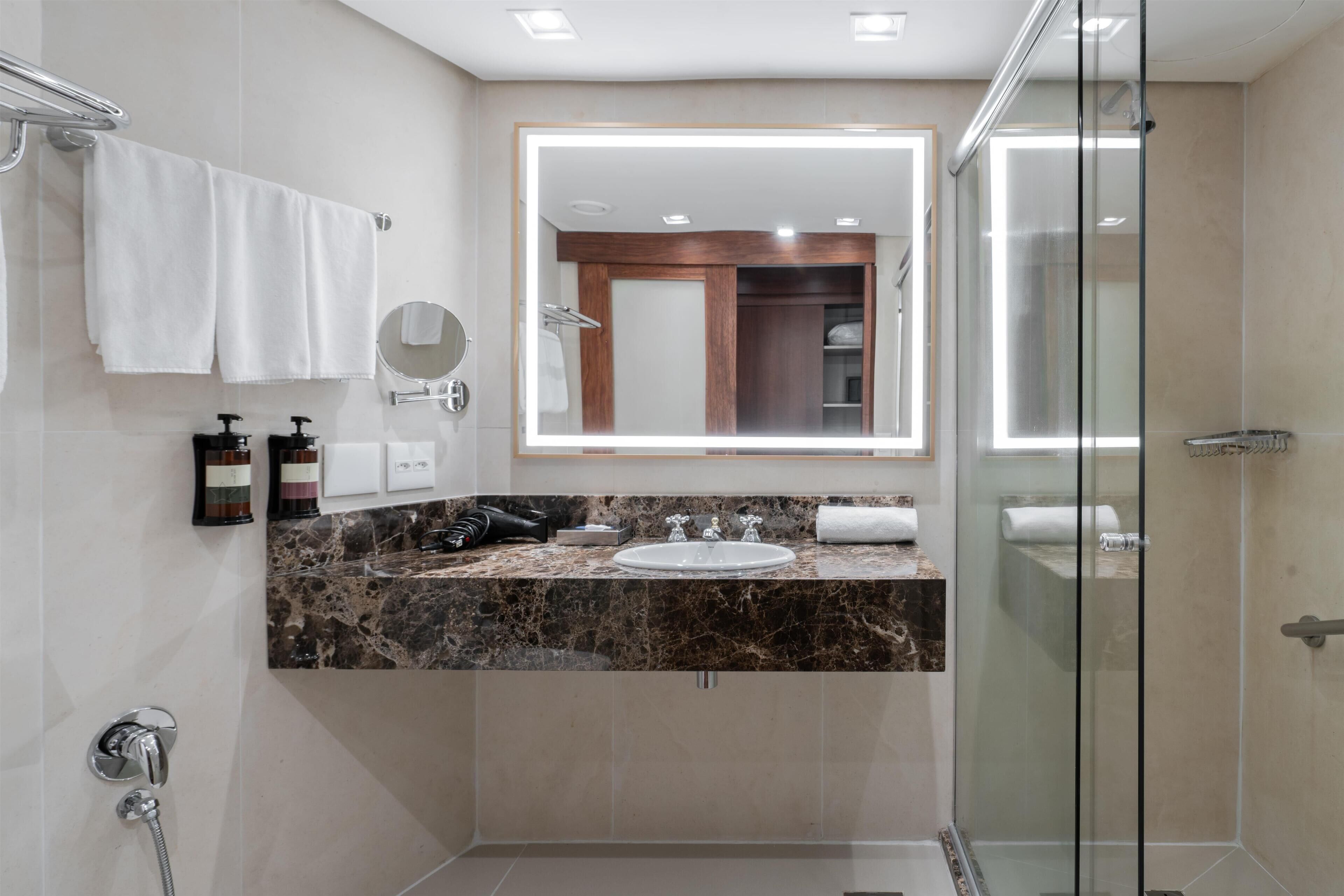 A modern bathroom with a marble countertop, a large mirror, a glass shower enclosure, and a towel rack.