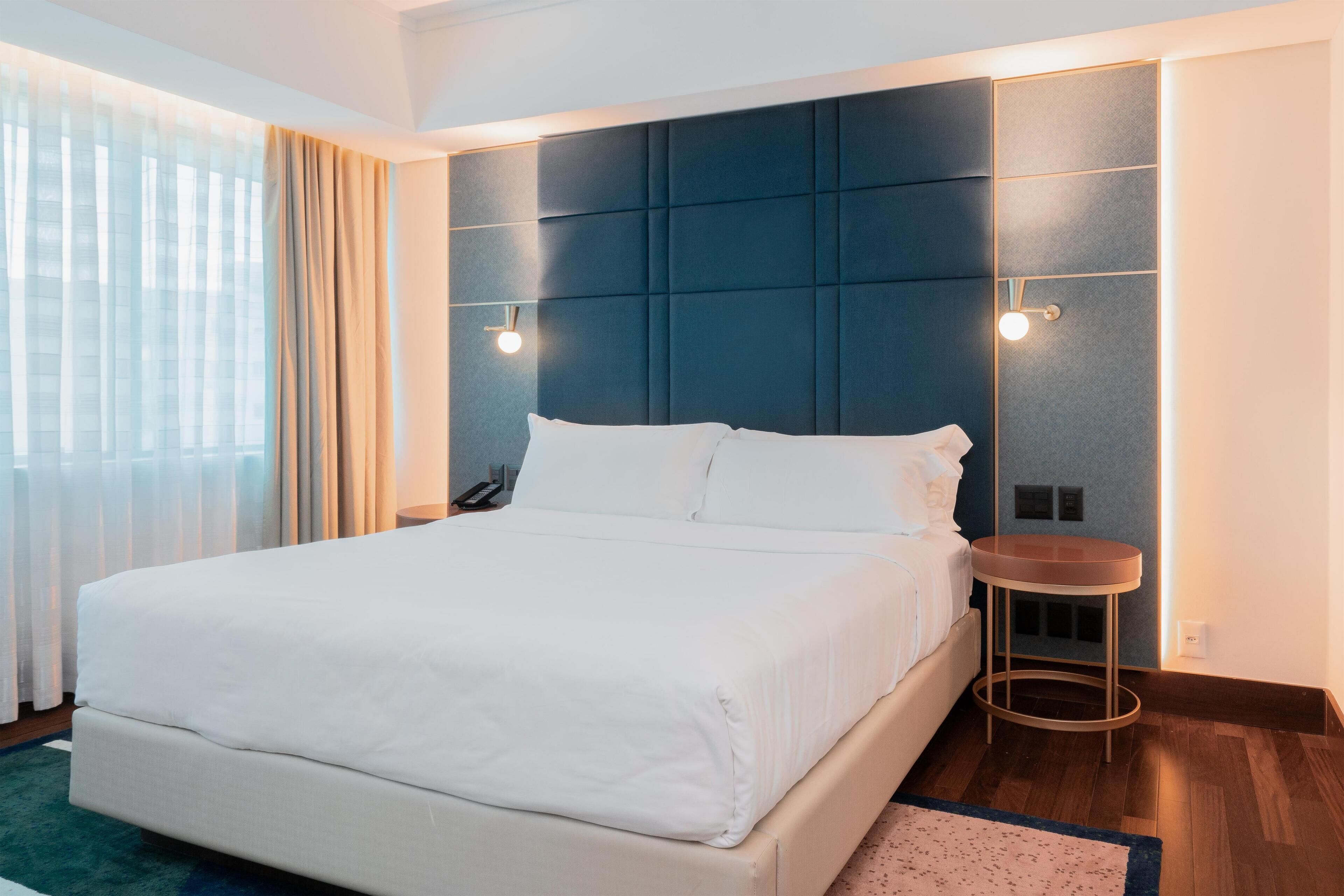 A modern hotel room with a large bed, a round side table, and a wall-mounted light fixture.