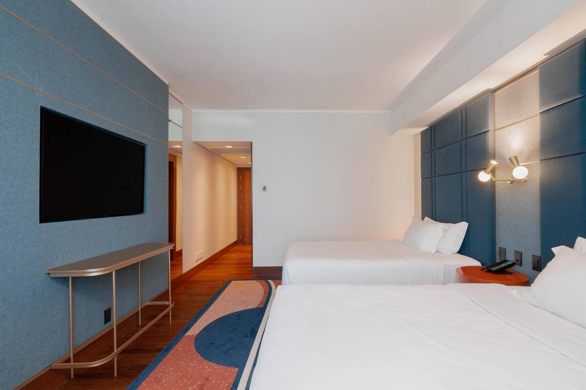 Een hotelkamer met twee bedden, een flatscreen televisie aan de muur, een klein tafeltje en een moderne lamp.