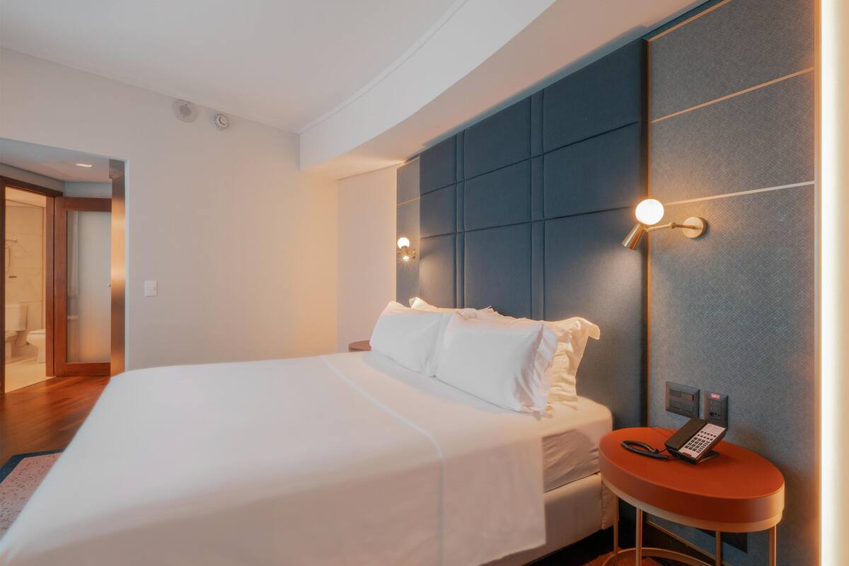 Een hotelkamer met een groot bed, een nachtkastje met een telefoon, en een wandlamp.
