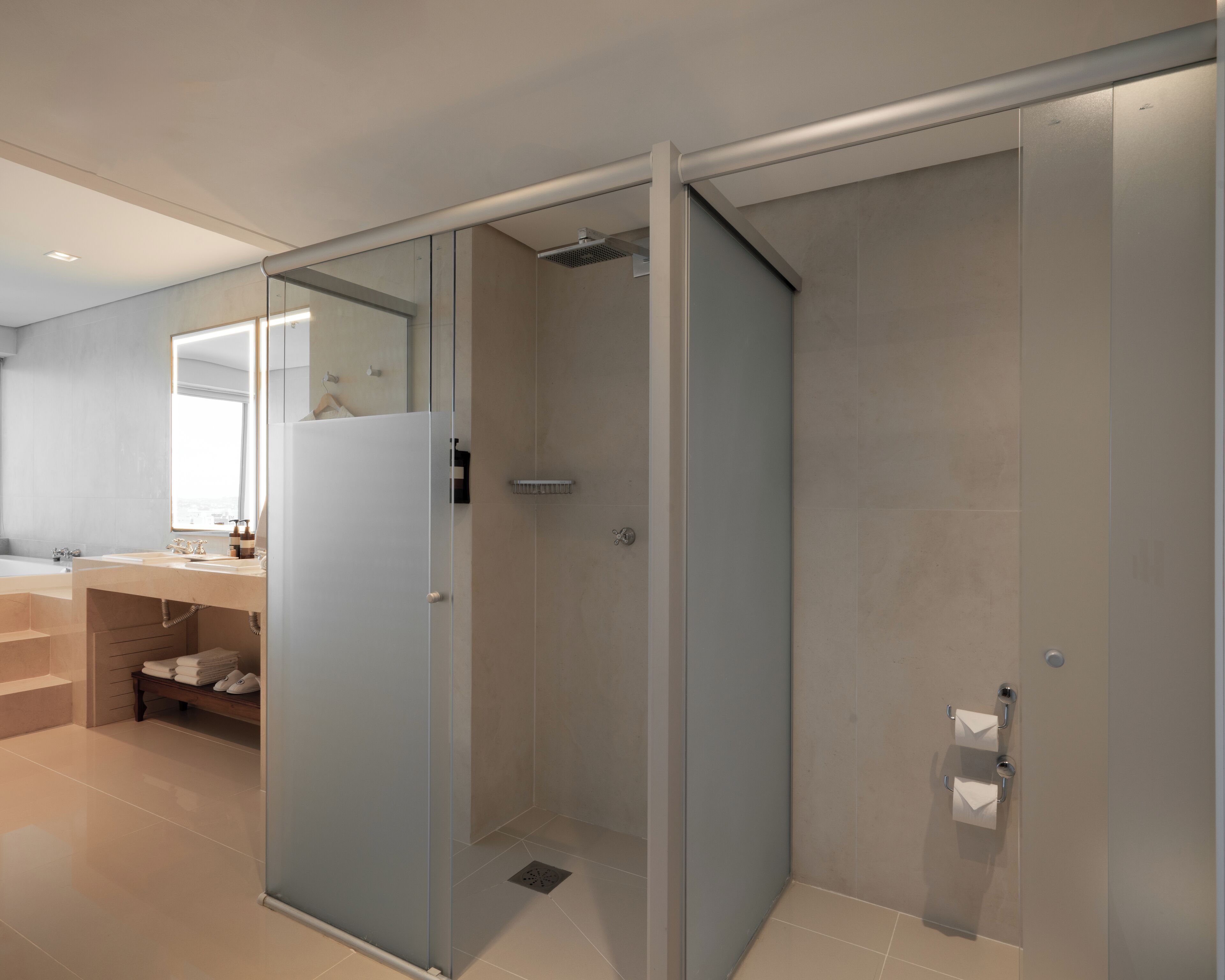 A modern bathroom with a glass shower enclosure, a vanity with a mirror, and a bench with towels.