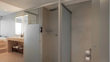 A modern bathroom with a glass shower enclosure, a vanity with a mirror, and a bench with towels.