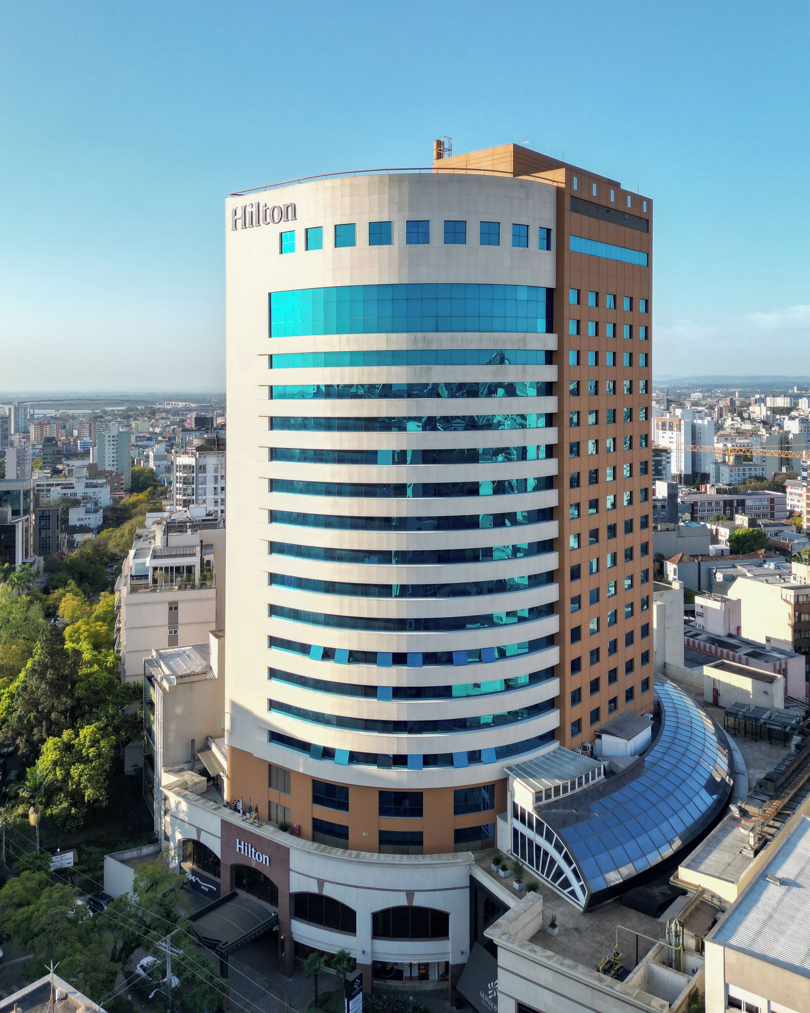 Um hotel moderno com fachada curva, vários andares e o logotipo Hilton em destaque.