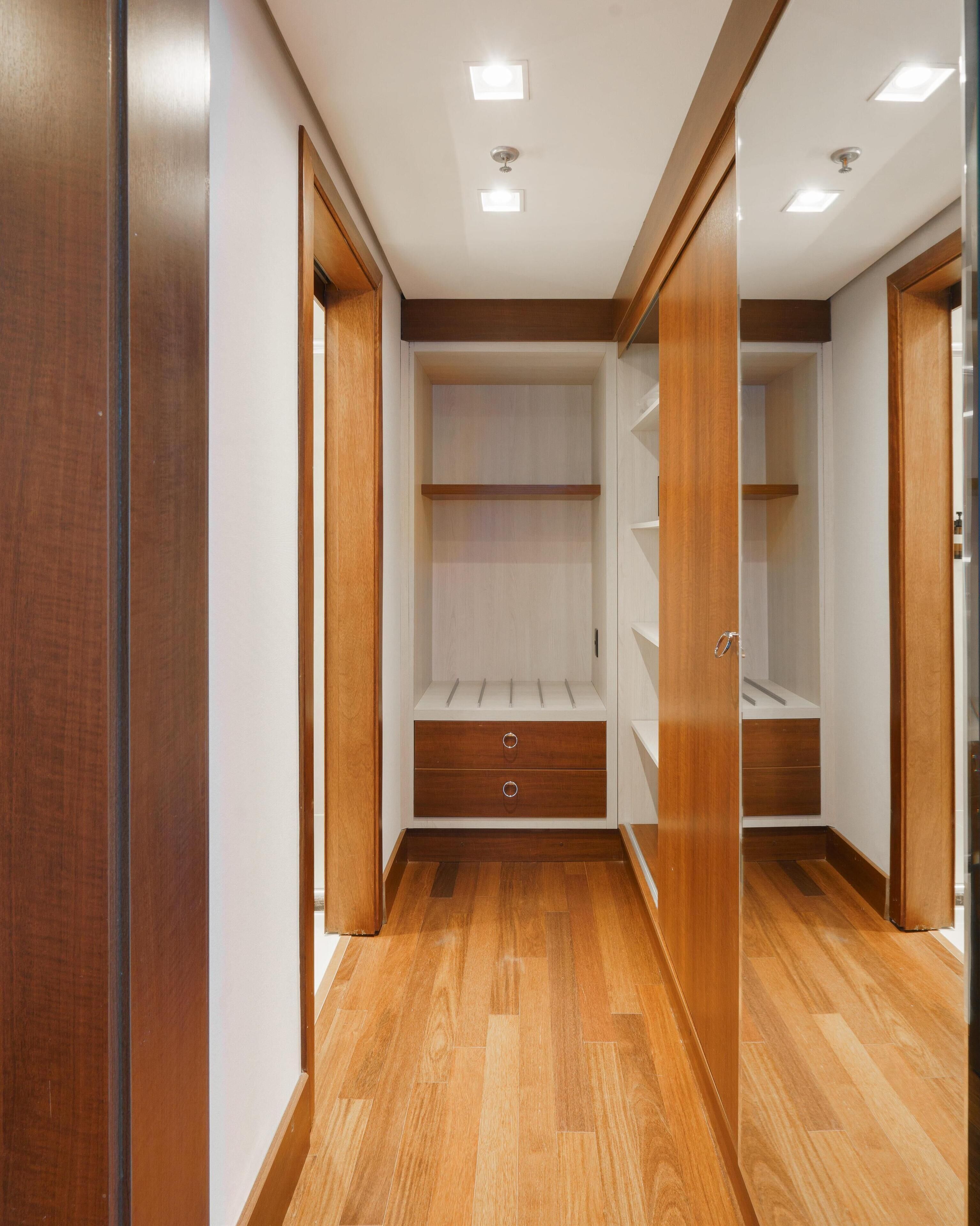 A walk-in closet with wooden flooring, built-in shelving, and a mirrored closet door.