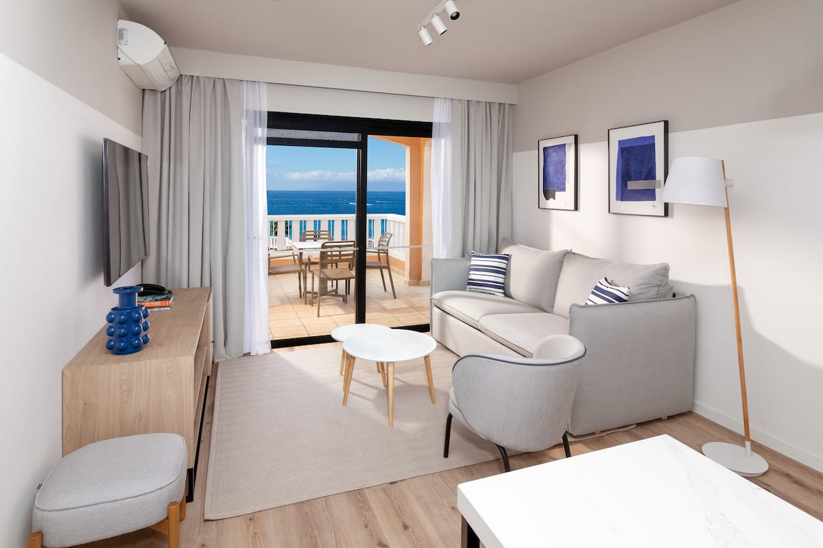 Quarto de hotel moderno com varanda, sofá, mesa de jantar e televisão.