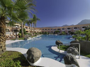 A resort pool with lounge chairs, palm trees, and a mountain backdrop. - Sol Sun Beach Apartamentos (Adeje)
