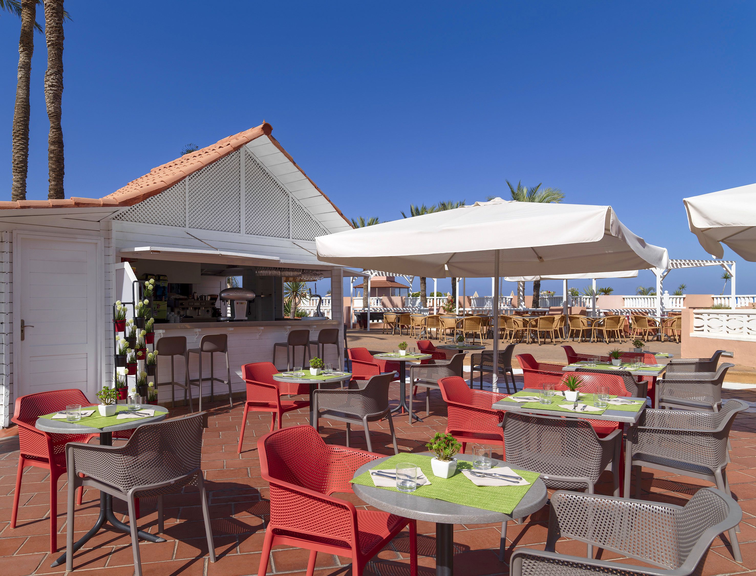 Un patio al aire libre con mesas, sillas, una zona de bar y sombrillas que dan sombra.