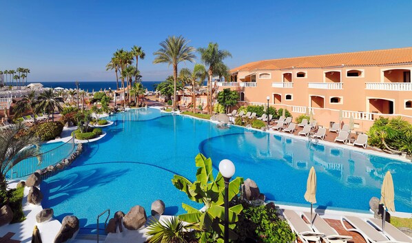 A resort pool with lounge chairs and palm trees. - Sol Sun Beach Apartamentos (Adeje)