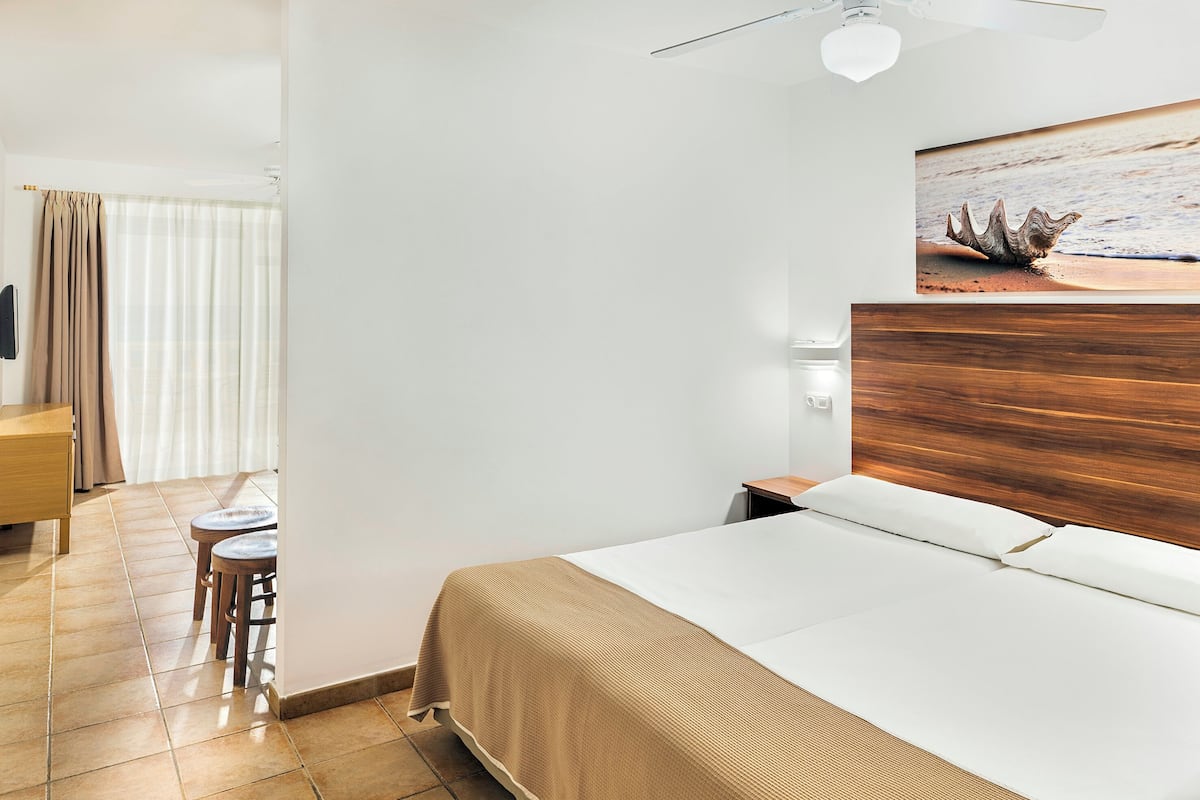 Quarto de hotel com cama, escrivaninha, cadeira e ventoinha no teto.