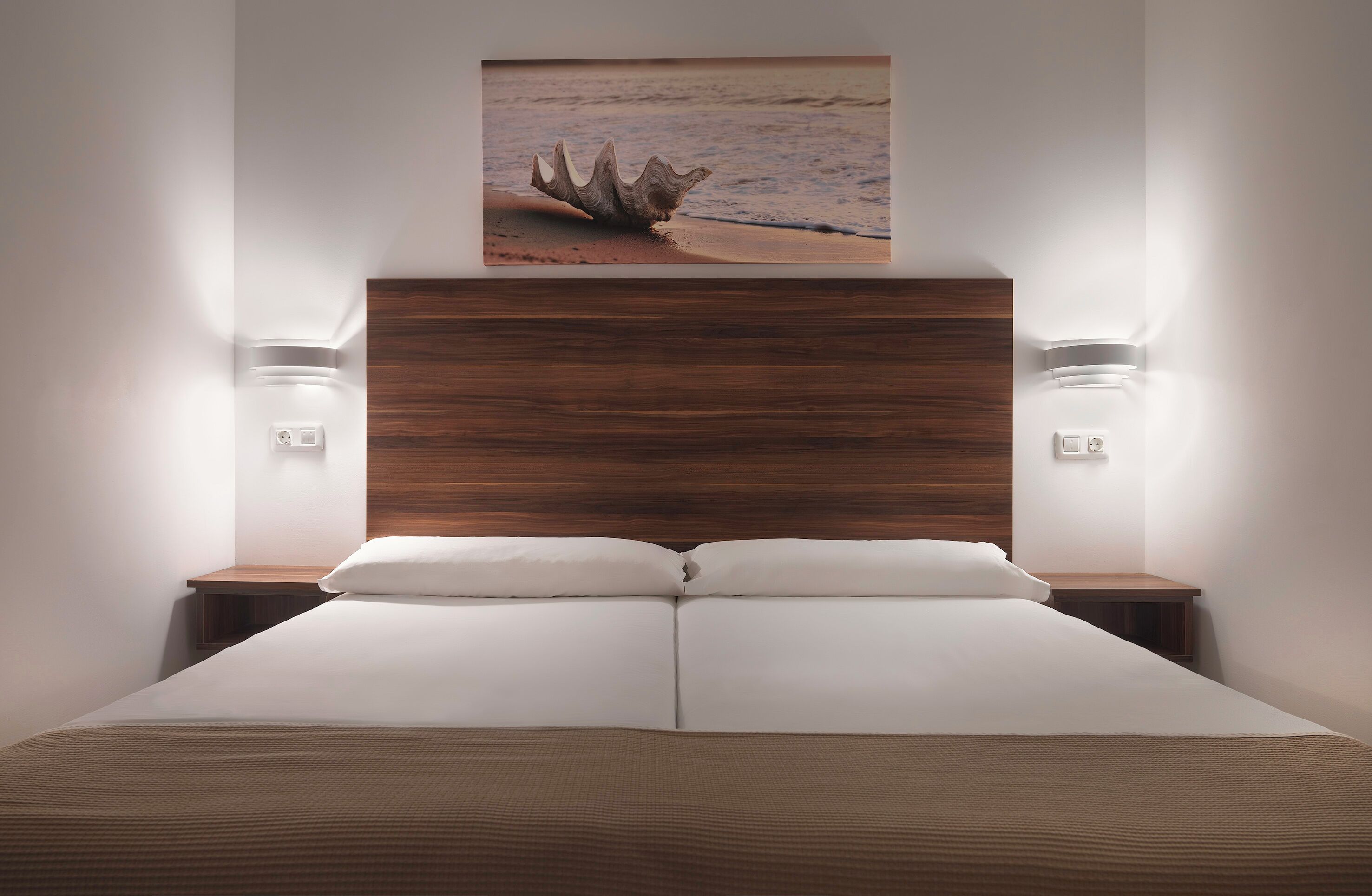 Camera da letto con una testiera in legno, due comodini con lampade e un letto grande con biancheria da letto bianca.