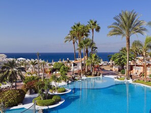 Een zwembadgedeelte van een resort met palmbomen, ligbedden en uitzicht op de oceaan.