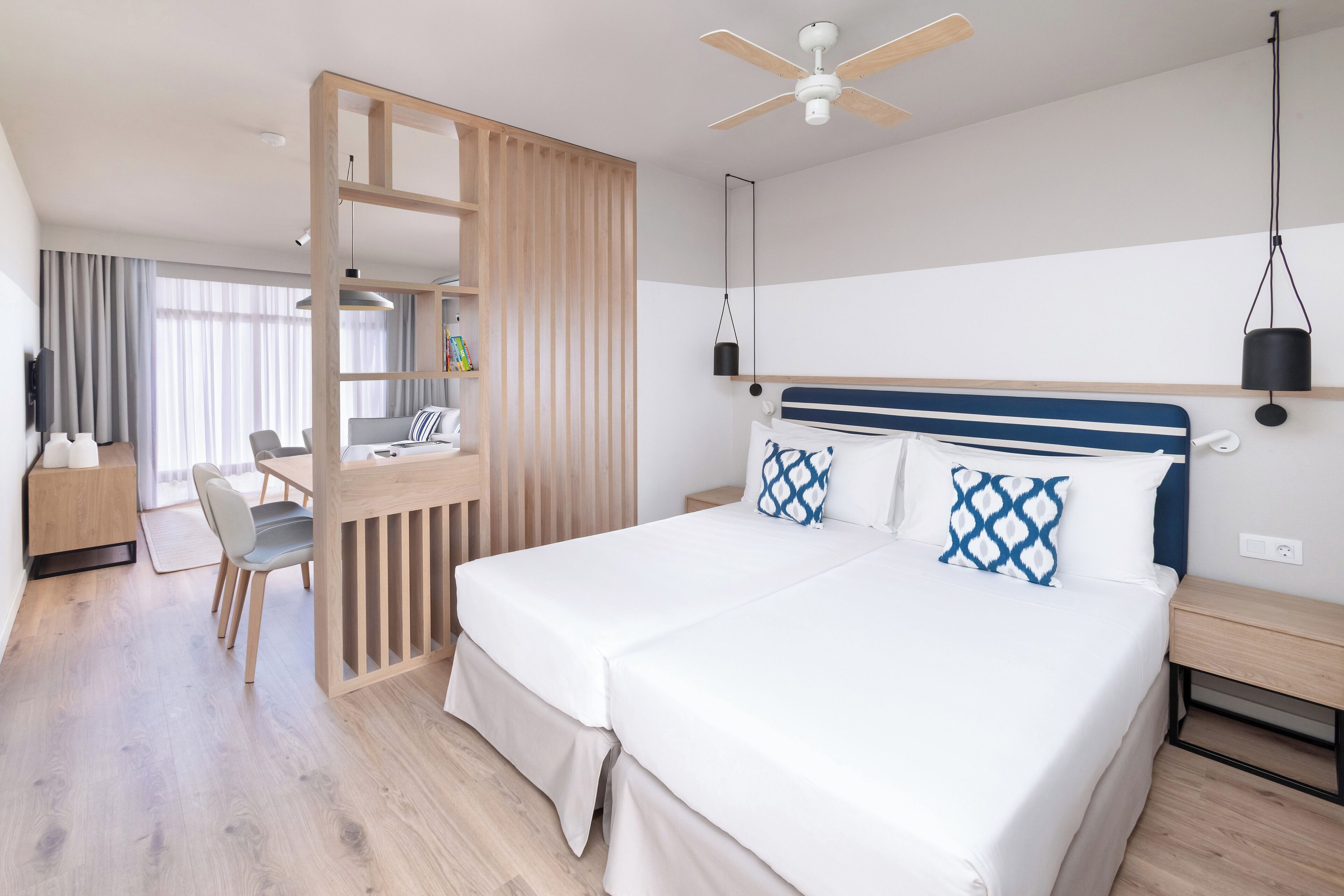 A hotel room with a bed, desk, chair, and a ceiling fan.