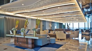 A modern lobby with a reception desk, seating area, and large windows offering a view of the sea.