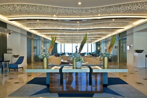 Un hall d’entrée spacieux avec un comptoir d’accueil central, un espace salon et un plafond décoratif agrémenté d’éléments suspendus.