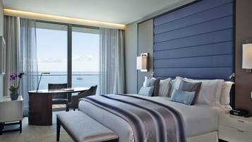 A hotel room with a large bed, a desk, and a view of the sea.