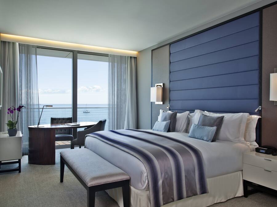A hotel room with a large bed, a desk, and a view of the sea.
