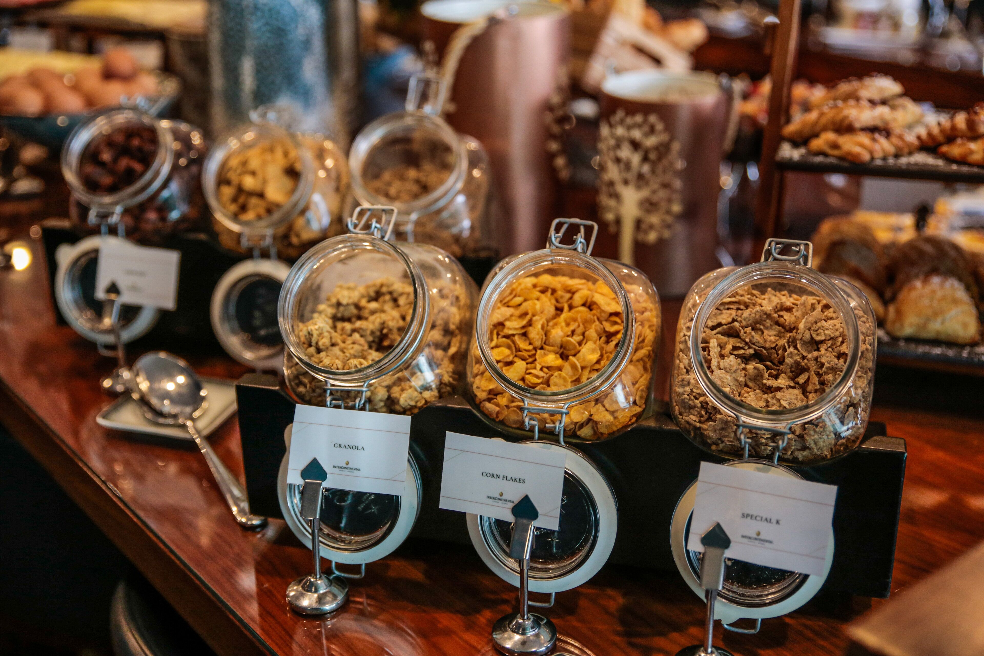 Een buffet met diverse etenswaren in glazen recipiënten, waaronder granola en maïsflakes.