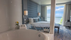 Une chambre d’hôtel moderne dotée d’une grande baignoire, d’un lit parfaitement fait, d’une vue sur la mer et d’un balcon avec un espace repas.