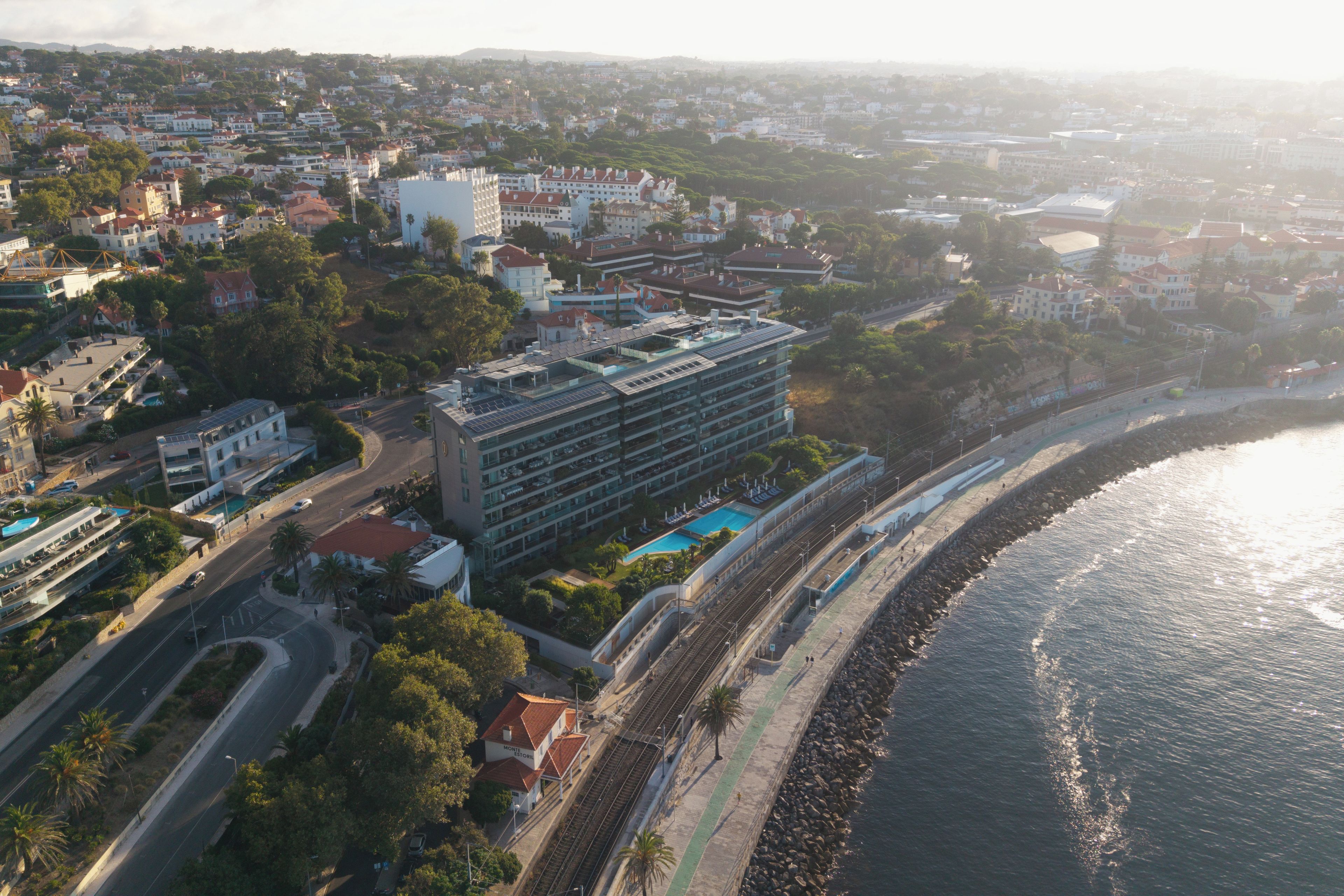 Une vue aérienne d’une ville côtière, avec un hôtel imposant doté d’une piscine sur le toit et d’une longue promenade le long du littoral.