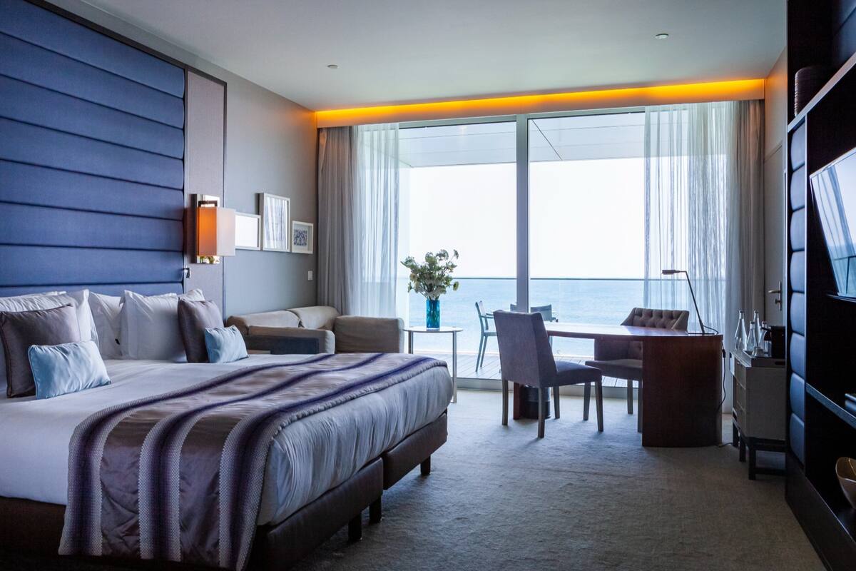 Ein Hotelzimmer mit einem großen Bett, einem Schreibtisch und einem Stuhl in der Nähe eines Fensters mit Meerblick.