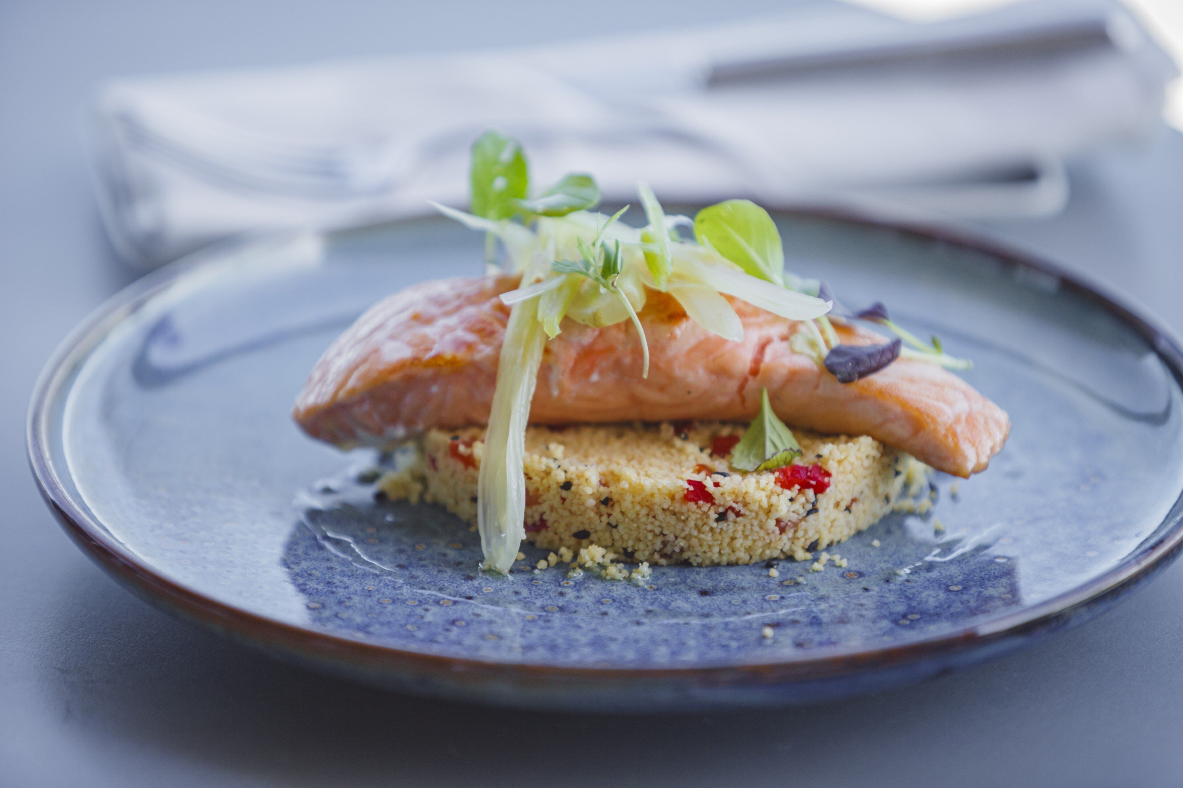 A plate with a salmon fillet, greens, and a grain-based dish.