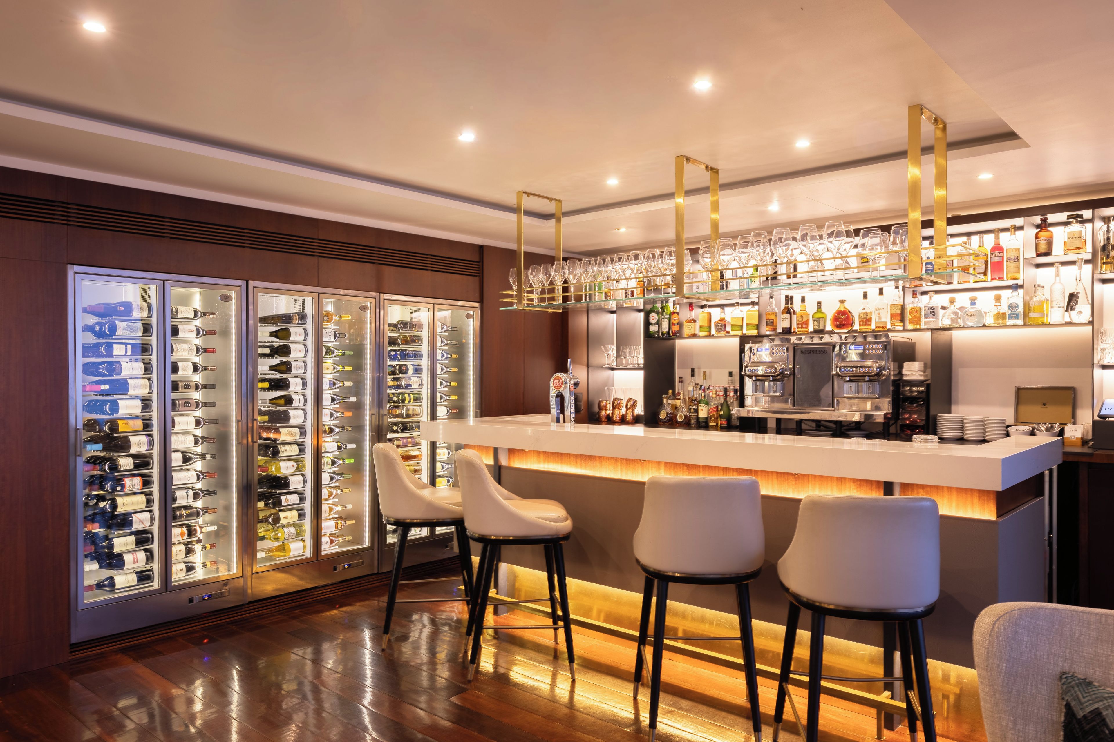 Una zona de bar con mostrador, taburetes y un enfriador de vino con botellas.