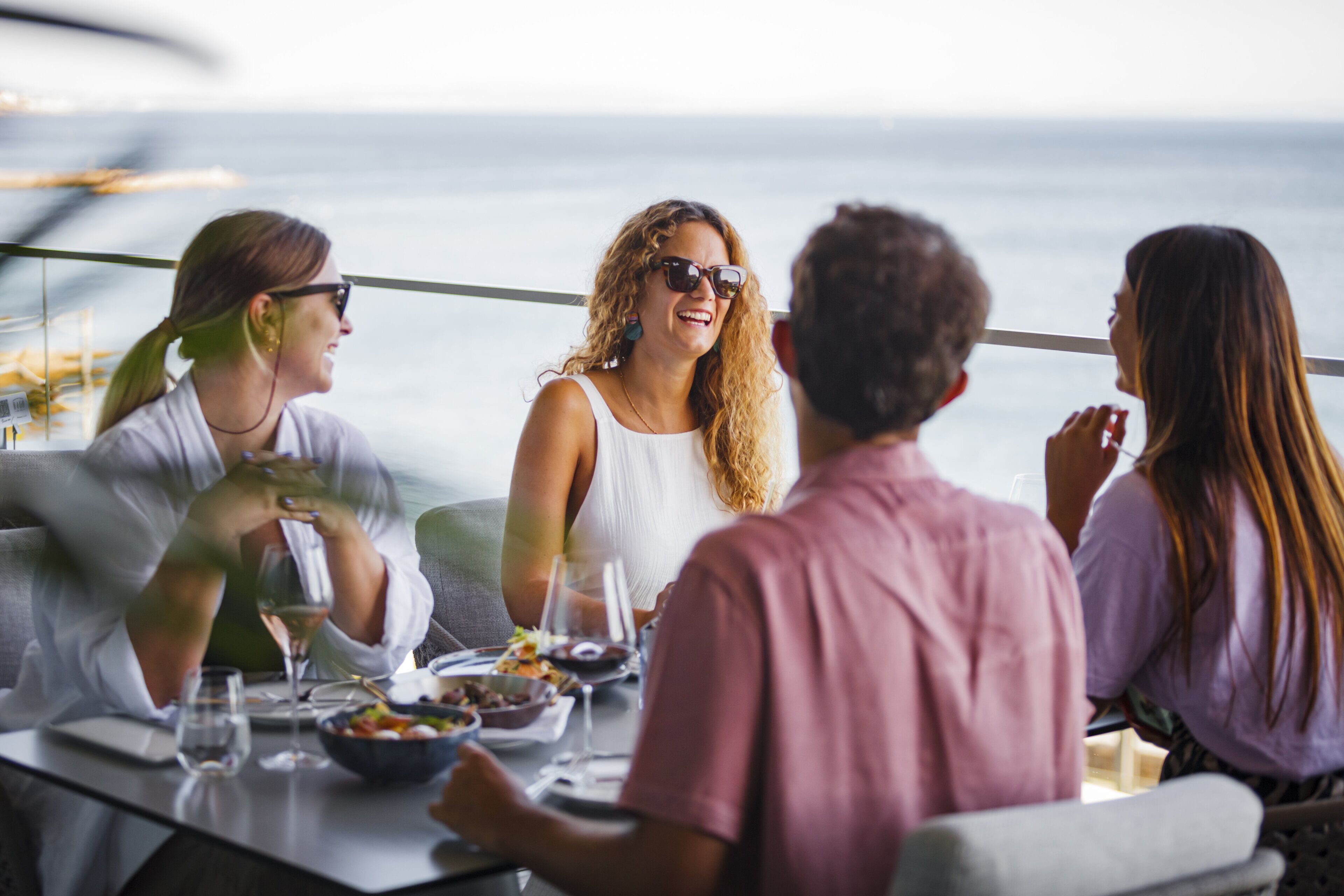 Un grupo de personas cenando en una mesa al aire libre con vistas al océano.