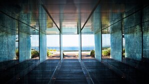 Un bâtiment moderne doté de grandes fenêtres en verre et d’un plancher en bois, qui donne sur un espace extérieur offrant une vue sur la mer.