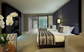 A hotel room with a large bed, a seating area, a TV, and a bathroom visible through a glass door.