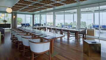 Una sala de conferencias moderna con una larga mesa, múltiples sillas y ventanas amplias que dan a una vista del mar.