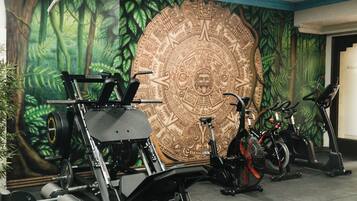 Uma academia com equipamentos de ginástica, incluindo uma estrutura para agachamento, um banco de supino e bicicletas ergométricas.