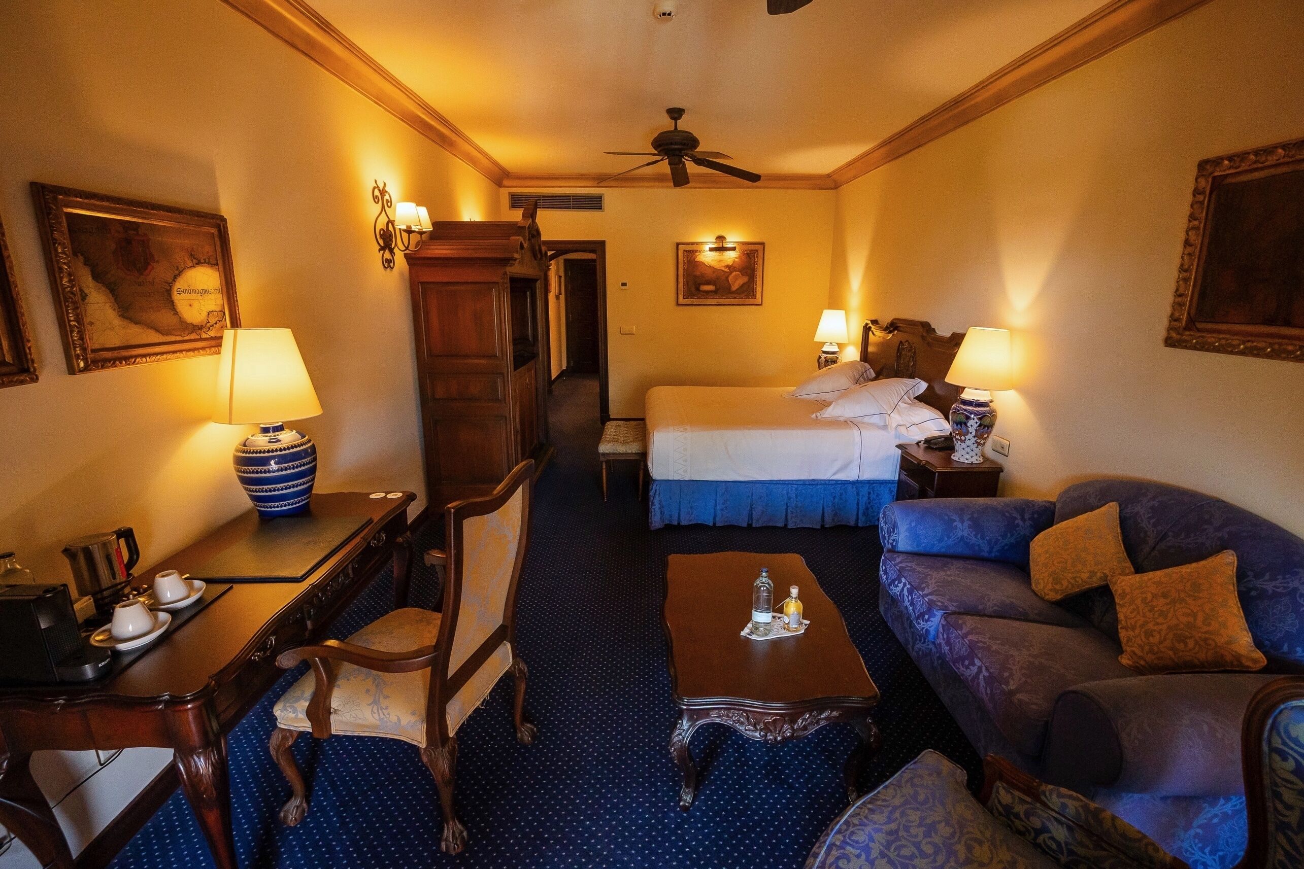 Une chambre d’hôtel équipée d’un lit, d’un canapé, d’un bureau avec une lampe, d’une chaise et d’un ventilateur de plafond.