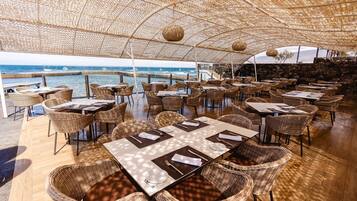 An outdoor dining area with wicker furniture and tables, overlooking the sea.