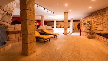 A spacious indoor area with stone pillars, yellow lounge chairs, and a tiled floor.