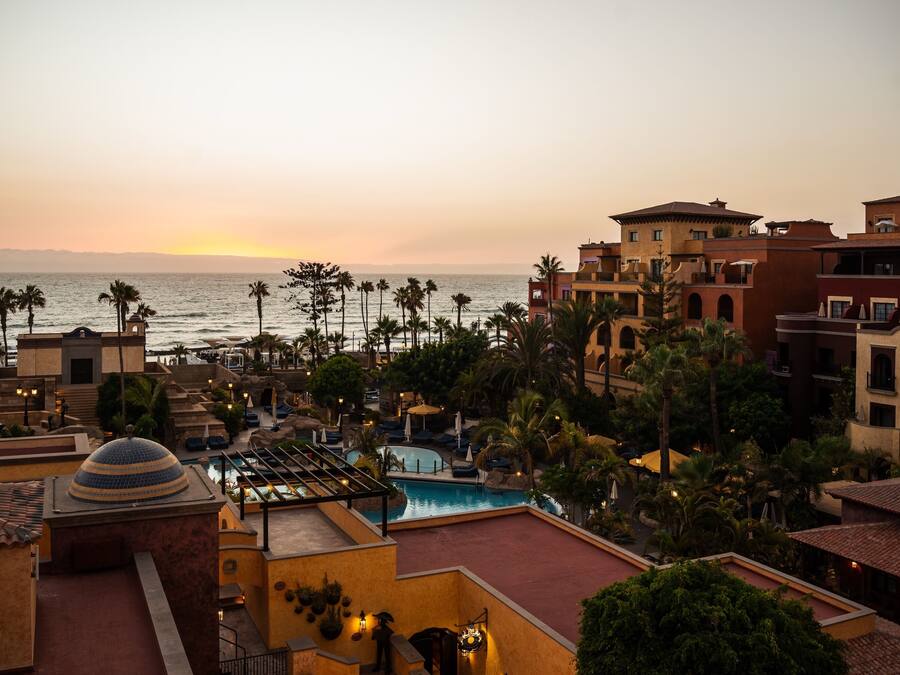 Een resort met een zwembad, palmbomen en uitzicht op de oceaan bij zonsondergang.
