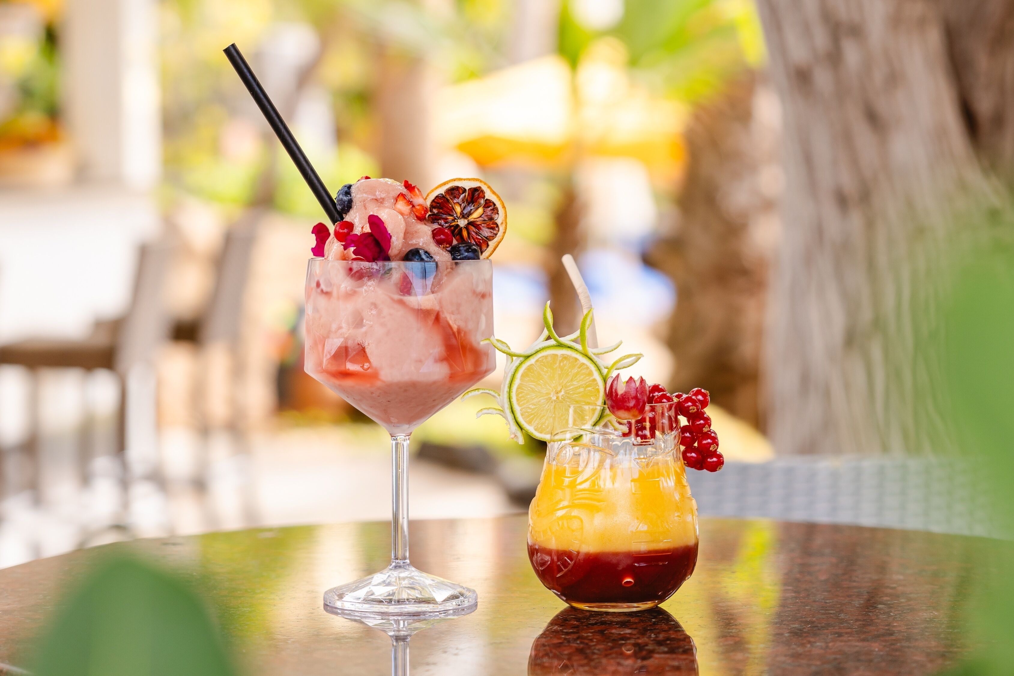 Two cocktails on a table with a blurred outdoor background.