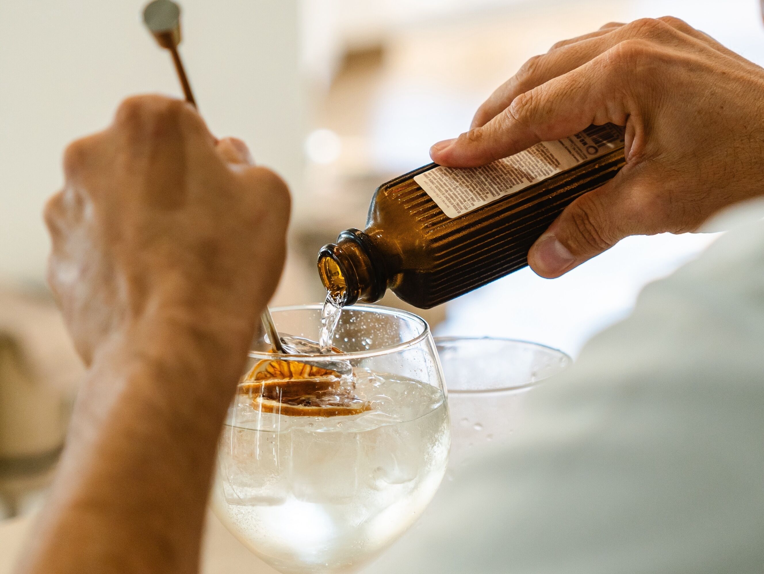 A person pouring a dark liquid into a clear glass with ice cubes.