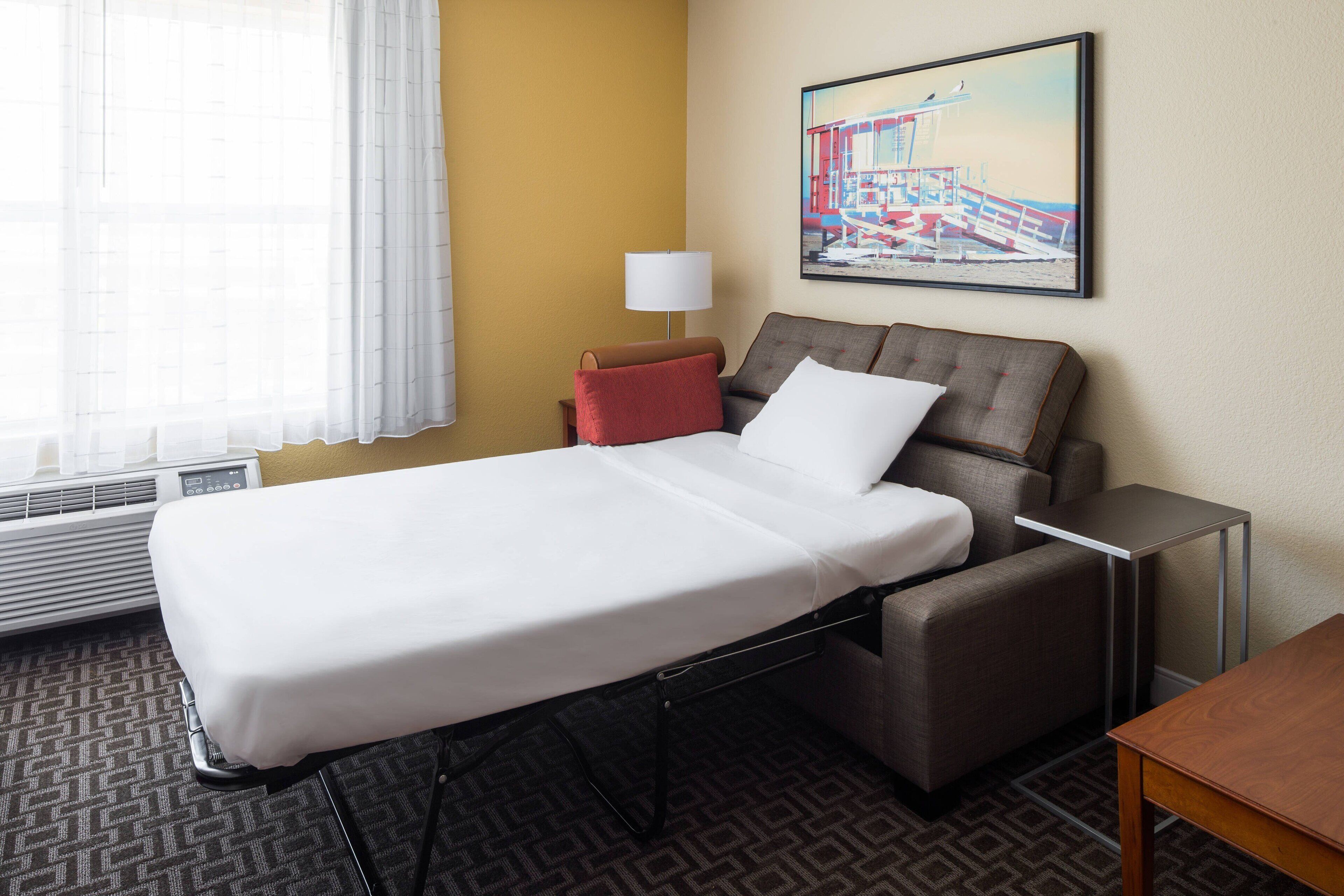 Une chambre d’hôtel avec un lit simple, un canapé, une petite table, une lampe et un tableau au mur.