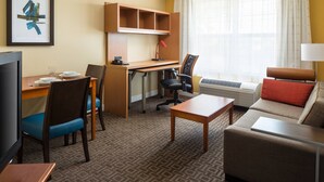 A hotel room with a desk, a chair, a sofa, a TV, and a window with curtains.