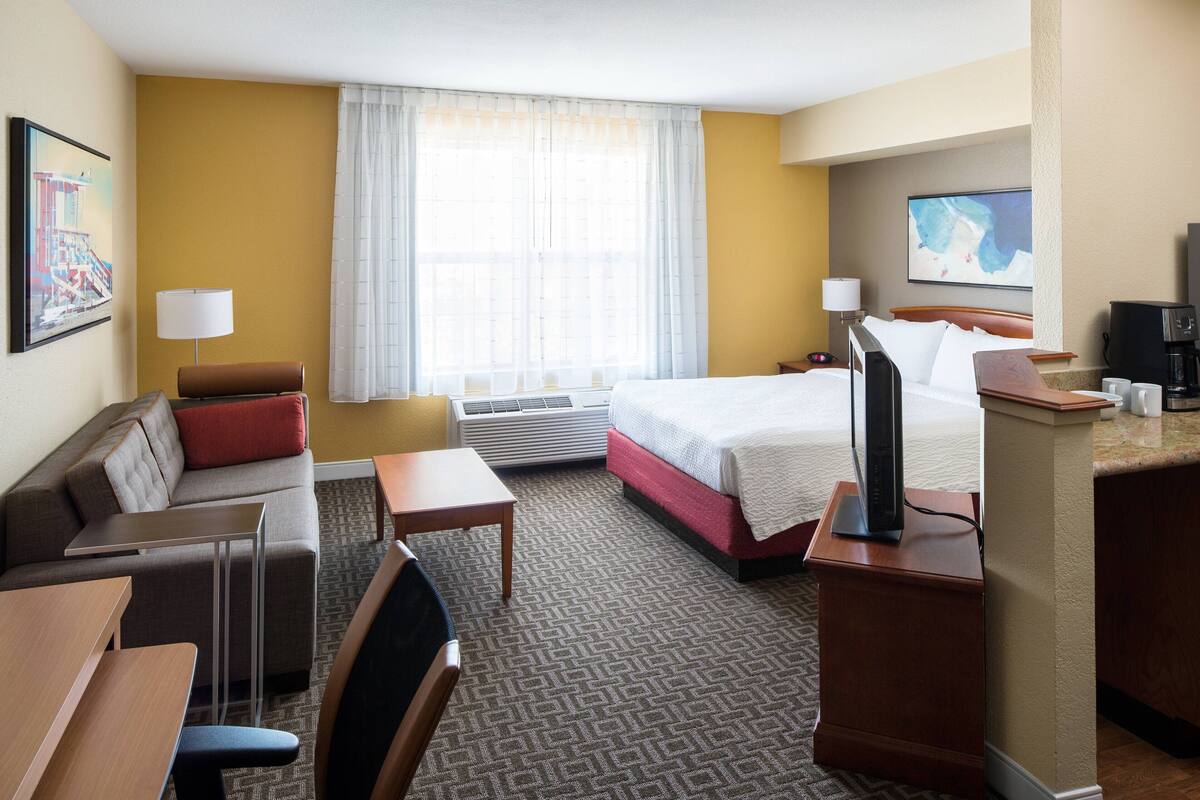 Une chambre d’hôtel équipée d’un lit, d’un bureau, d’une chaise, d’un canapé, d’une machine à café et d’une télévision.