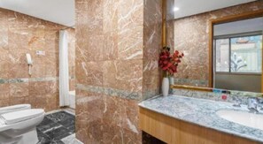 A bathroom with a marble wall, a sink, and a toilet. - Kunming Business Hotel (Kunming)