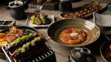 A variety of dishes on a wooden table, including grilled meat, sashimi, and other appetizers.