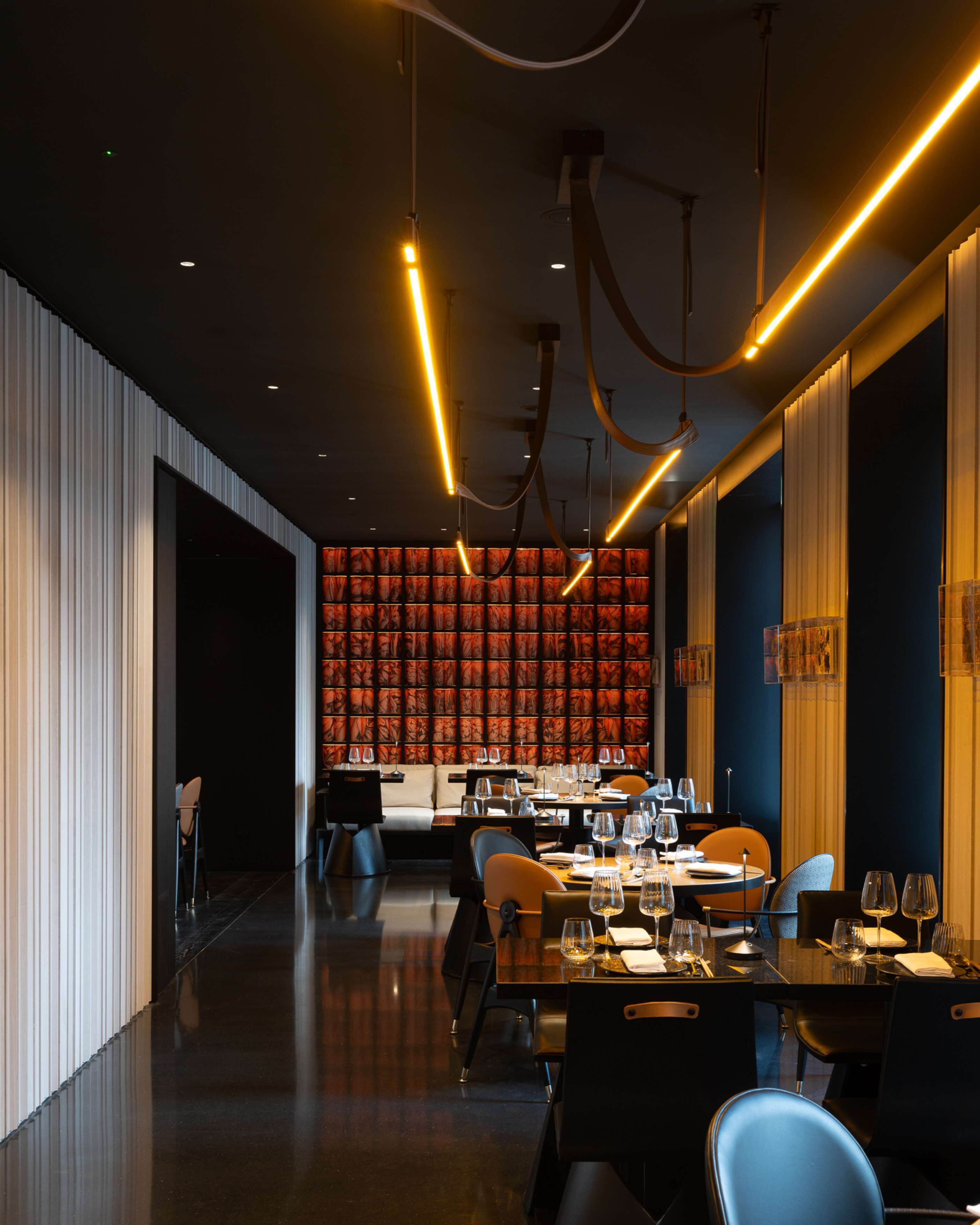 L’intérieur d’un restaurant moderne, avec une longue table à manger, des chaises et un mur à motifs en arrière-plan.
