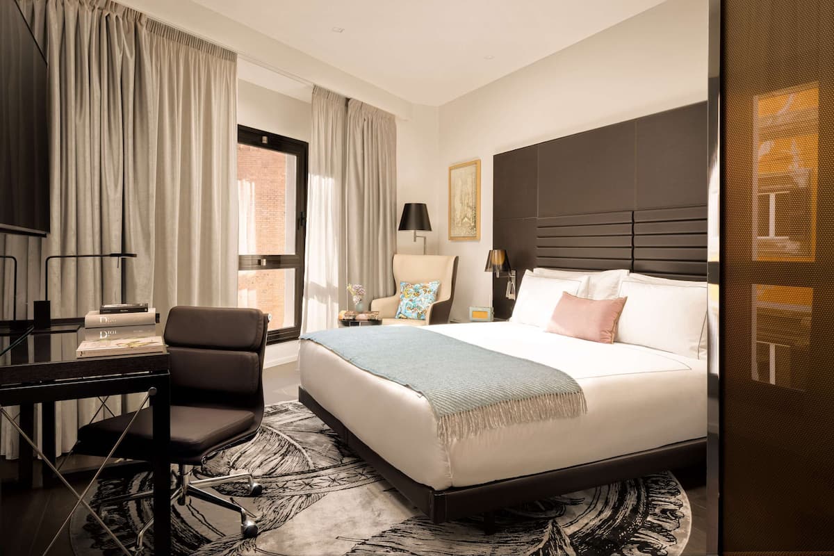 A hotel room with a large bed, a desk with a chair, a TV, and a window with curtains.