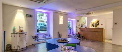 Un área de recepción con un escritorio de madera, asientos azules y una ventana que da a coches aparcados.