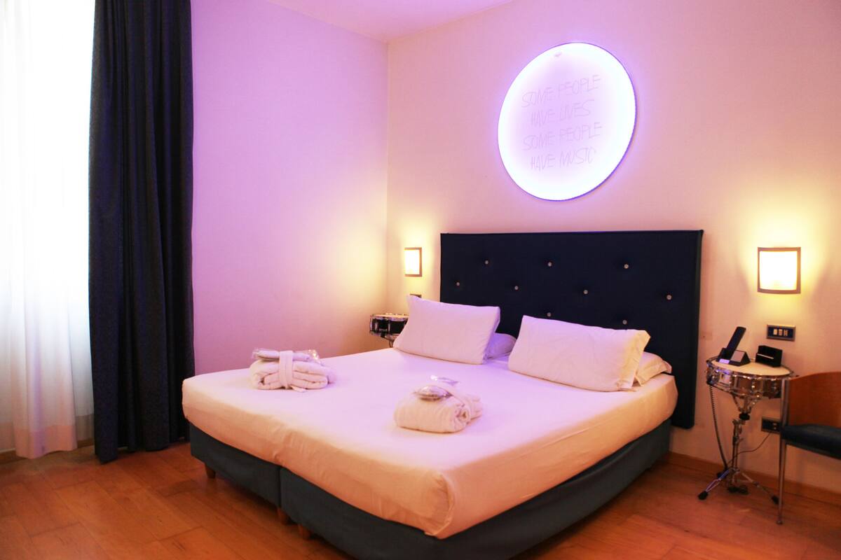 A hotel room with a large bed, two bedside tables, a round wall light, and a mirror.