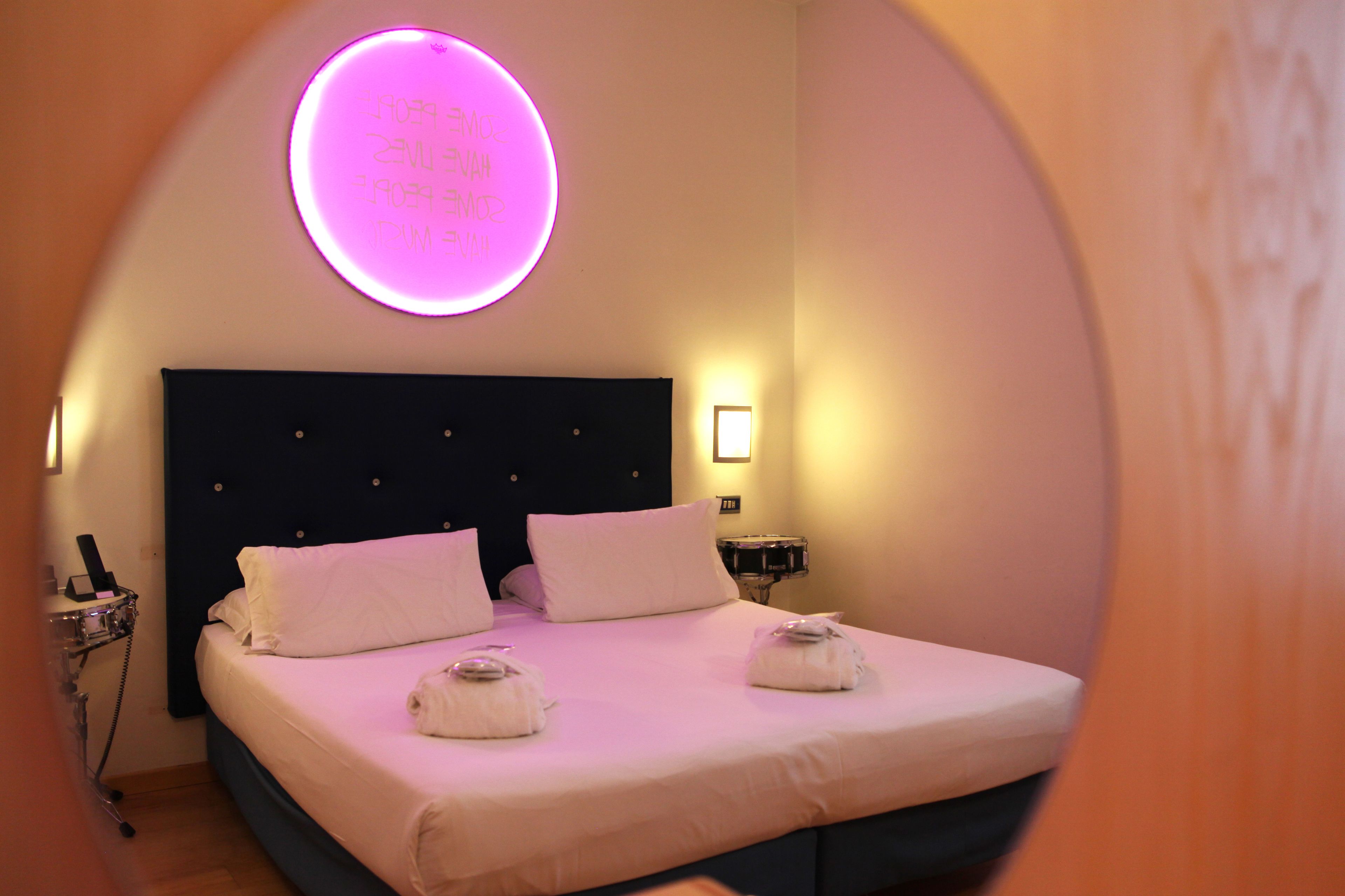 A hotel room with a bed, pillows, and a neon sign on the wall.