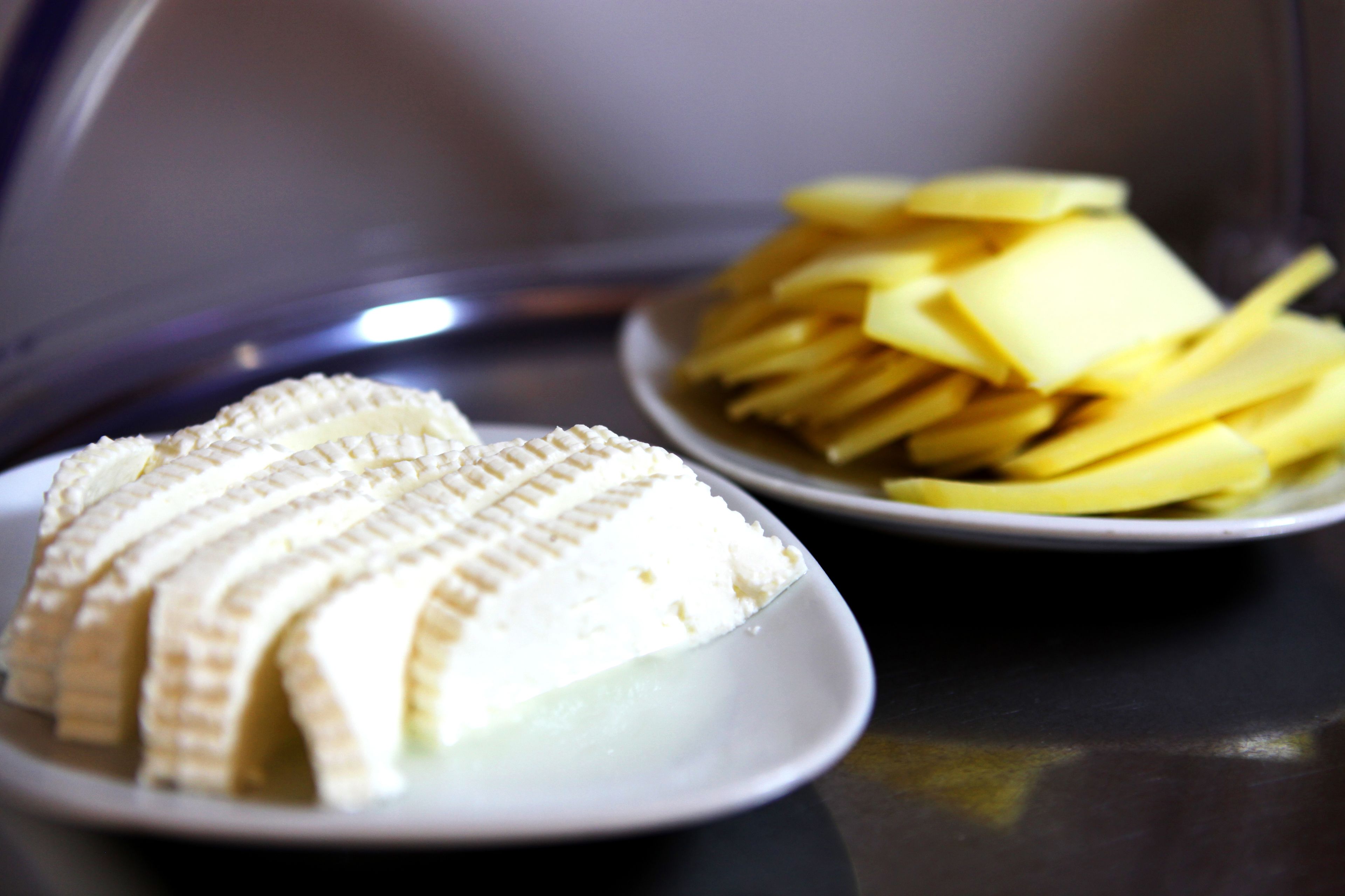 Duas travessas brancas com bananas fatiadas e queijo sobre uma superfície refletora.