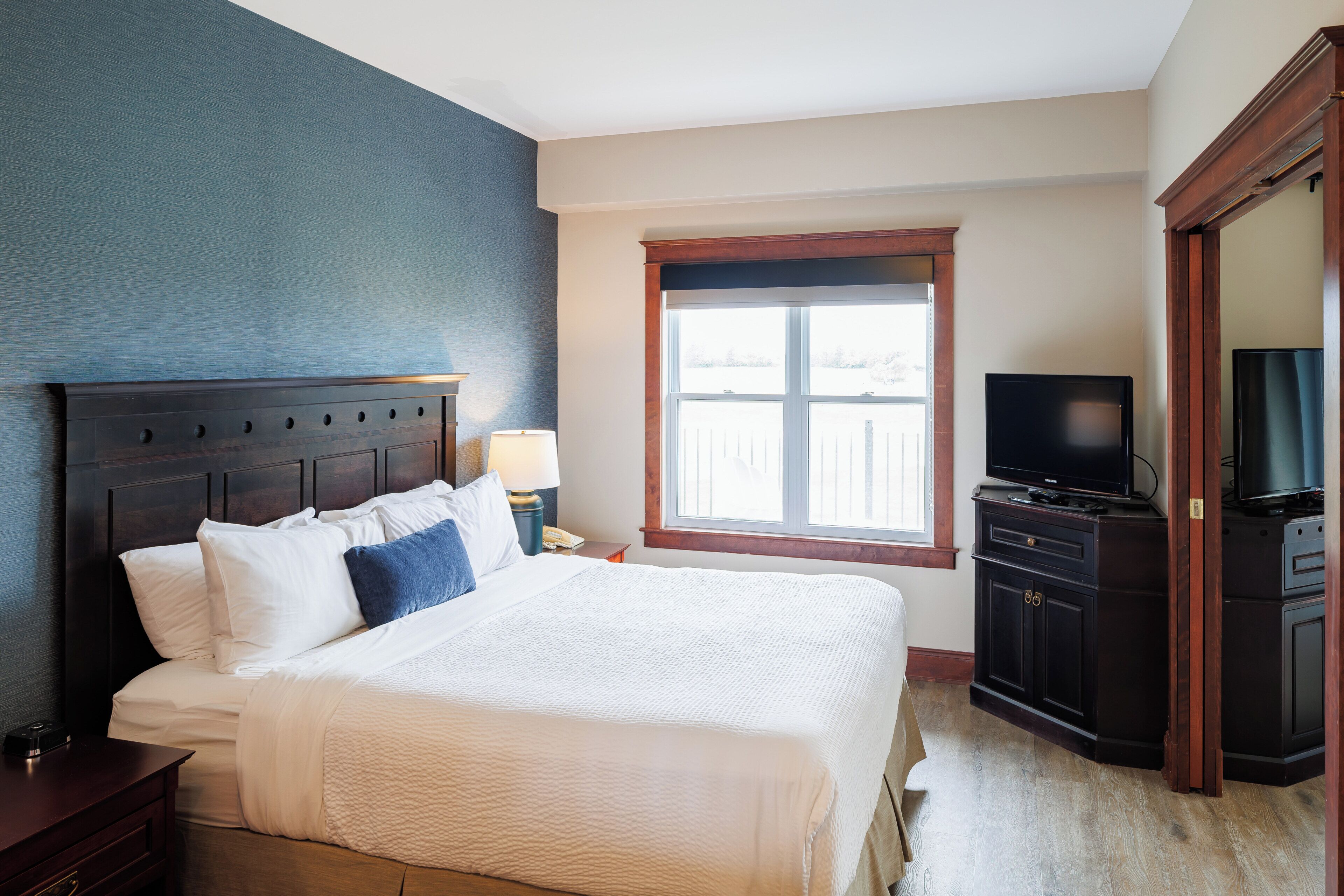 A hotel room with a large bed, a television, a wardrobe, and a window with a view.