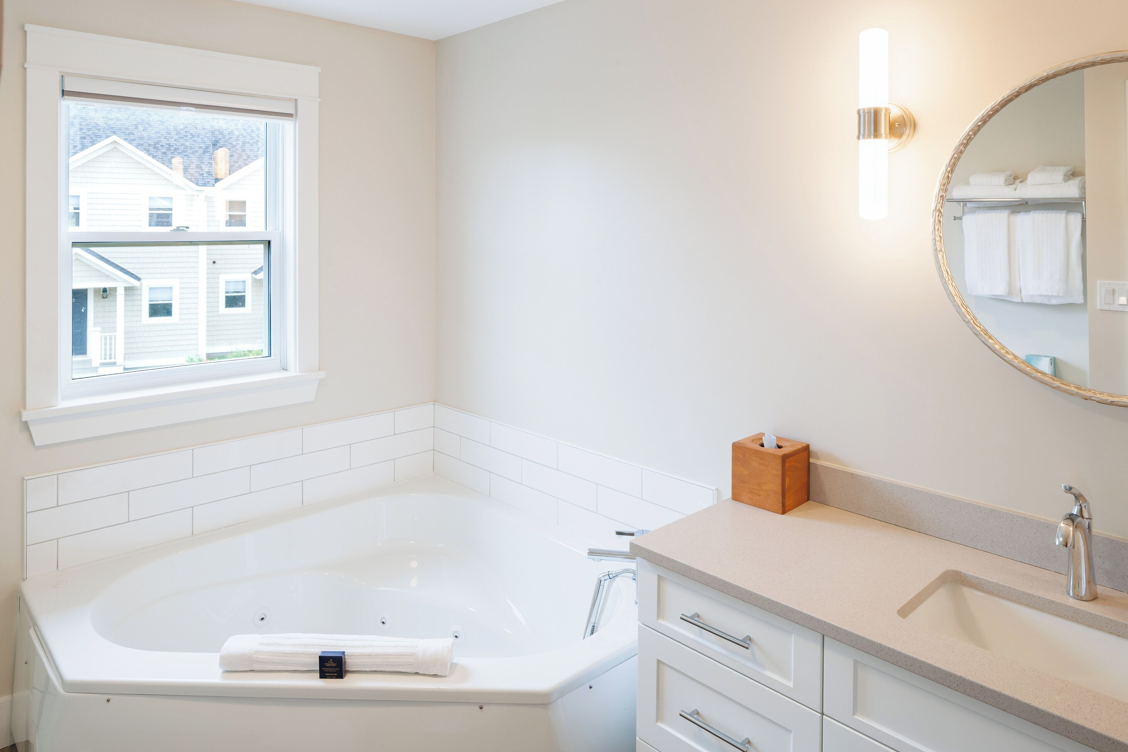 A modern bathroom with a bathtub, a window, a vanity with a mirror, and a towel rack.